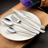Elegant silver cutlery set with curved handles arranged on textured plate beside lavender on wood board.